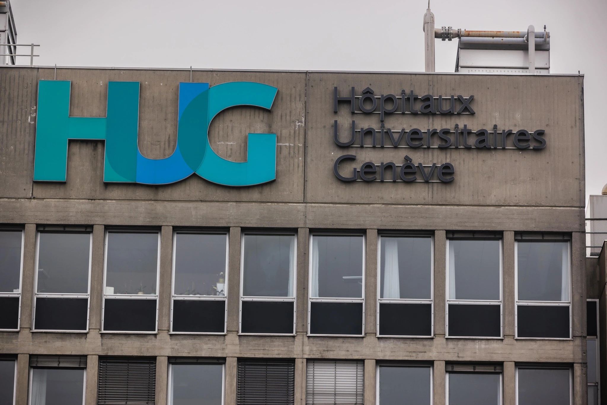 Facade of the Hôpitaux universitaires de Genève bearing the large HUG logo and the hospital name.